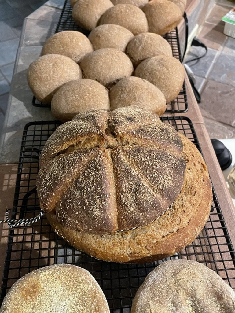 A batch of rolls and a round loaf cooling on racks.