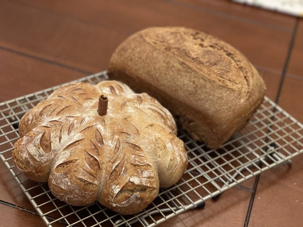 Pumpkin-shaped sourdough and a loaf cooling on a rack.