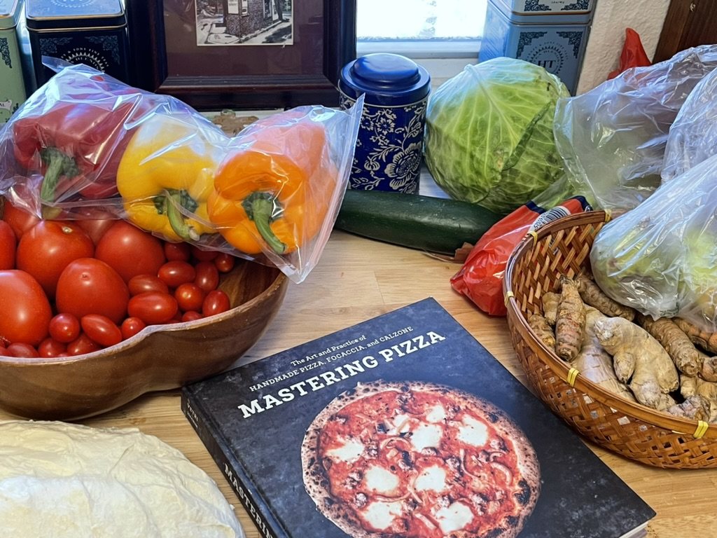 Produce, dough, and Mastering Pizza on a counter.