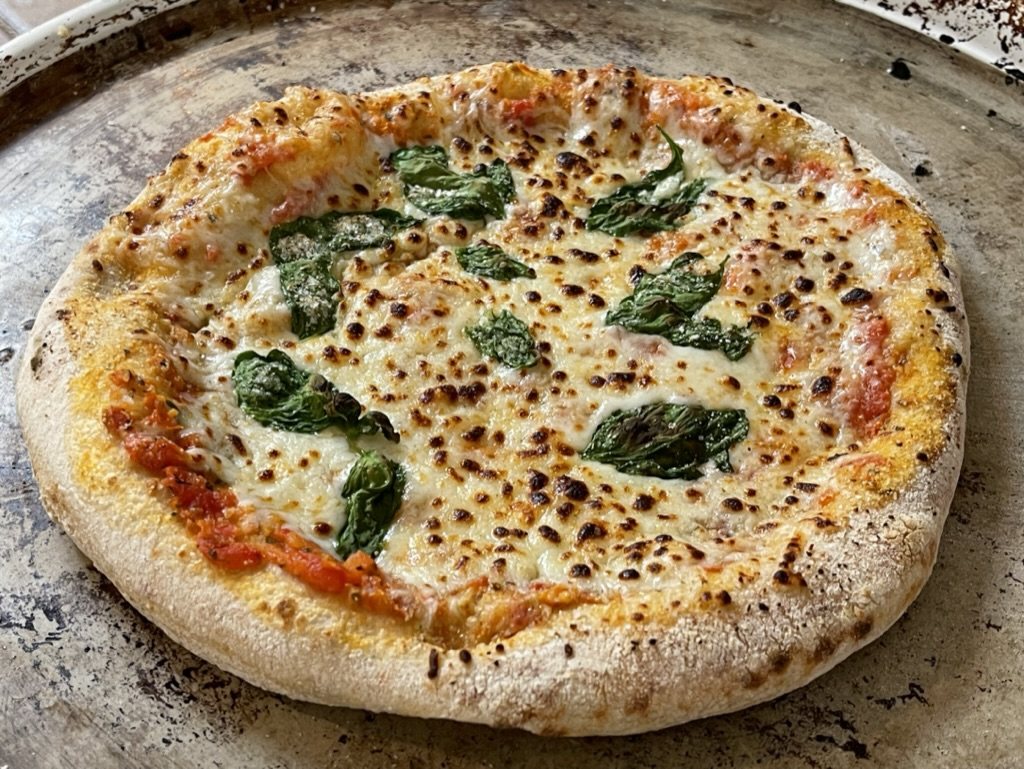 A finished pizza with blistered cheese and basil.